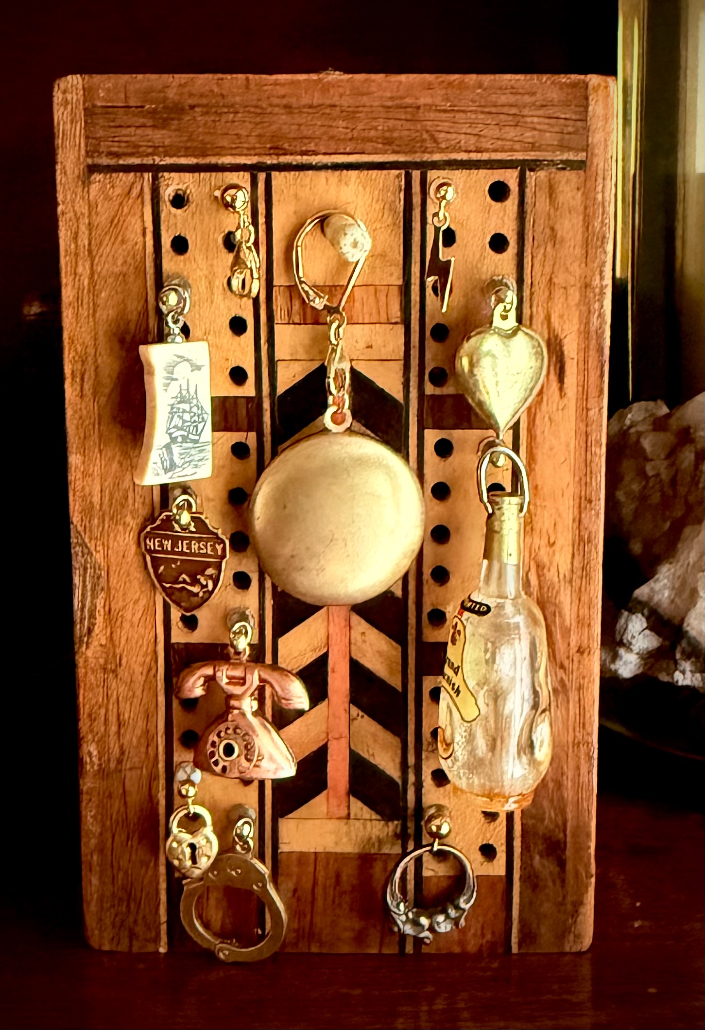 Latest Tiny Mischief collection displayed on a wooden board, including a telephone, bottle, New Jersey shield, sailing ship, handcuff, puffy brass heart, and Sidekicks